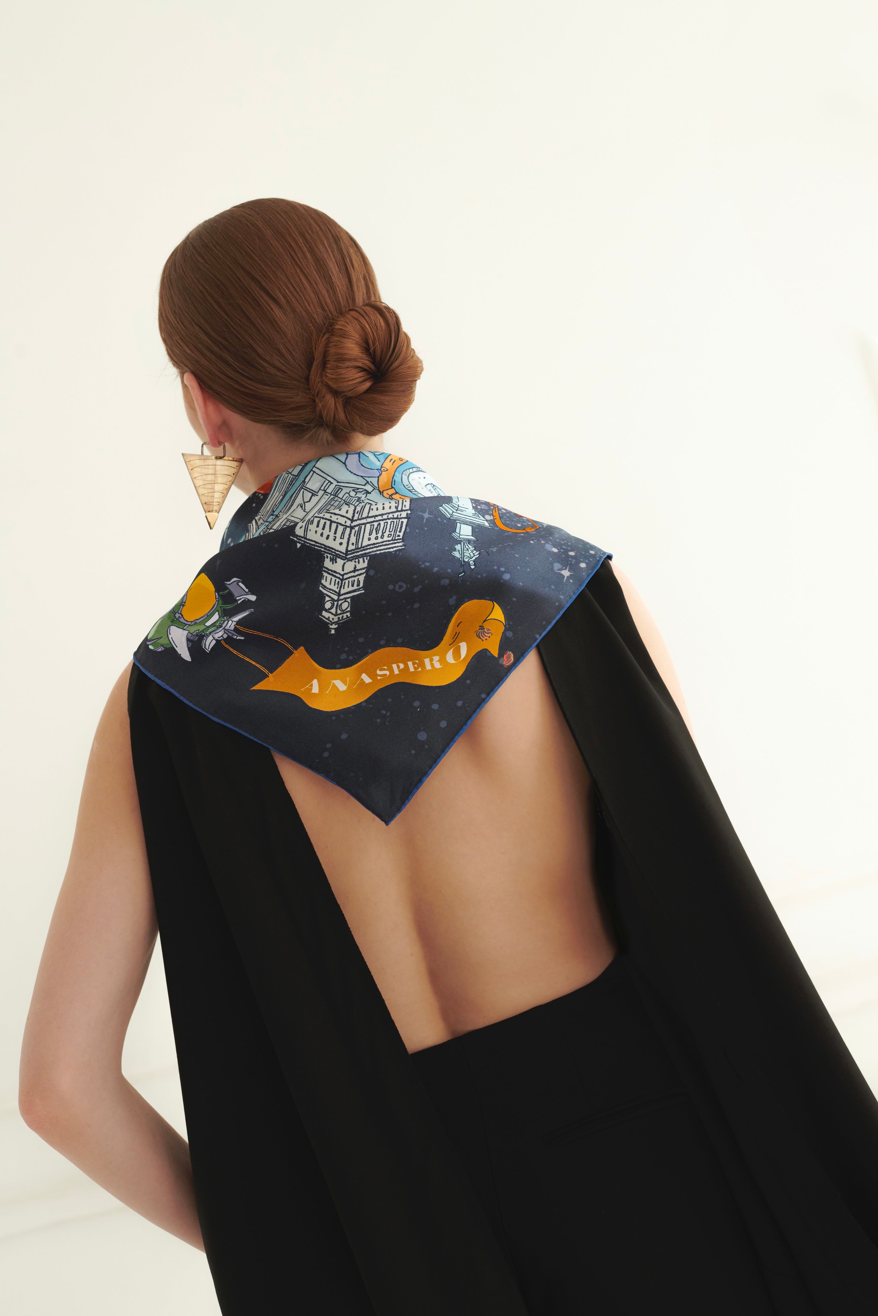 Woman wearing a black dress with an open back and a decorative scarf on her arms against a white background