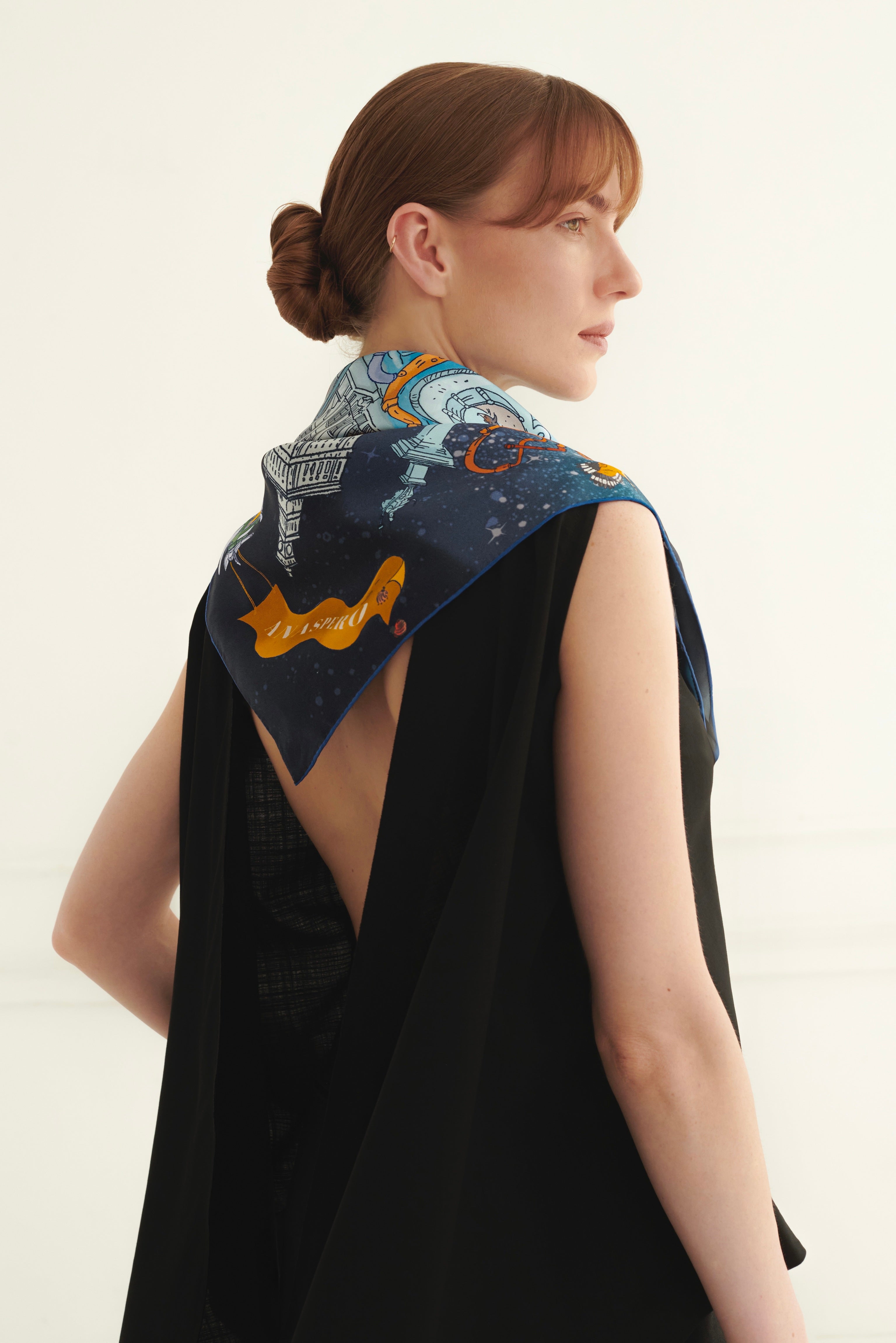 Woman wearing a black sleeveless top with a colorful scarf draped over her shoulders against a white background